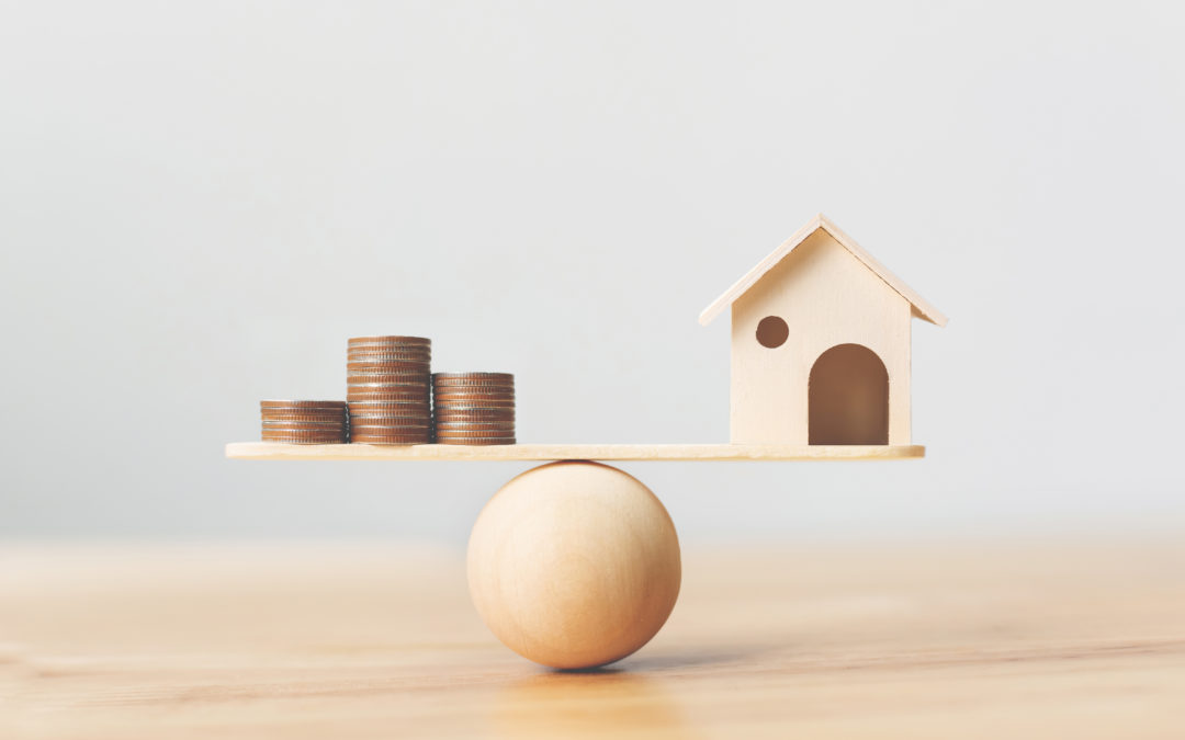 Wooden home and money coins stack on wood scale. Property investment and house mortgage financial real estate concept